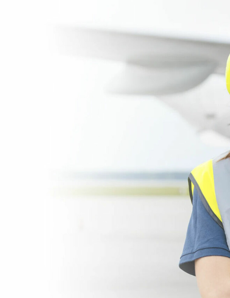 Kvinne, bakkepersonell, foran fly, gul refleksvest, hørselsvern.