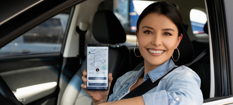 Kvinnelig, smilende sjåfør viser en app på mobilen