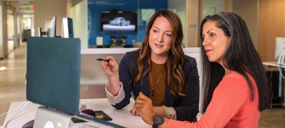 To kvinnelige ansatte diskuterer foran skjerme med et smil om munnen